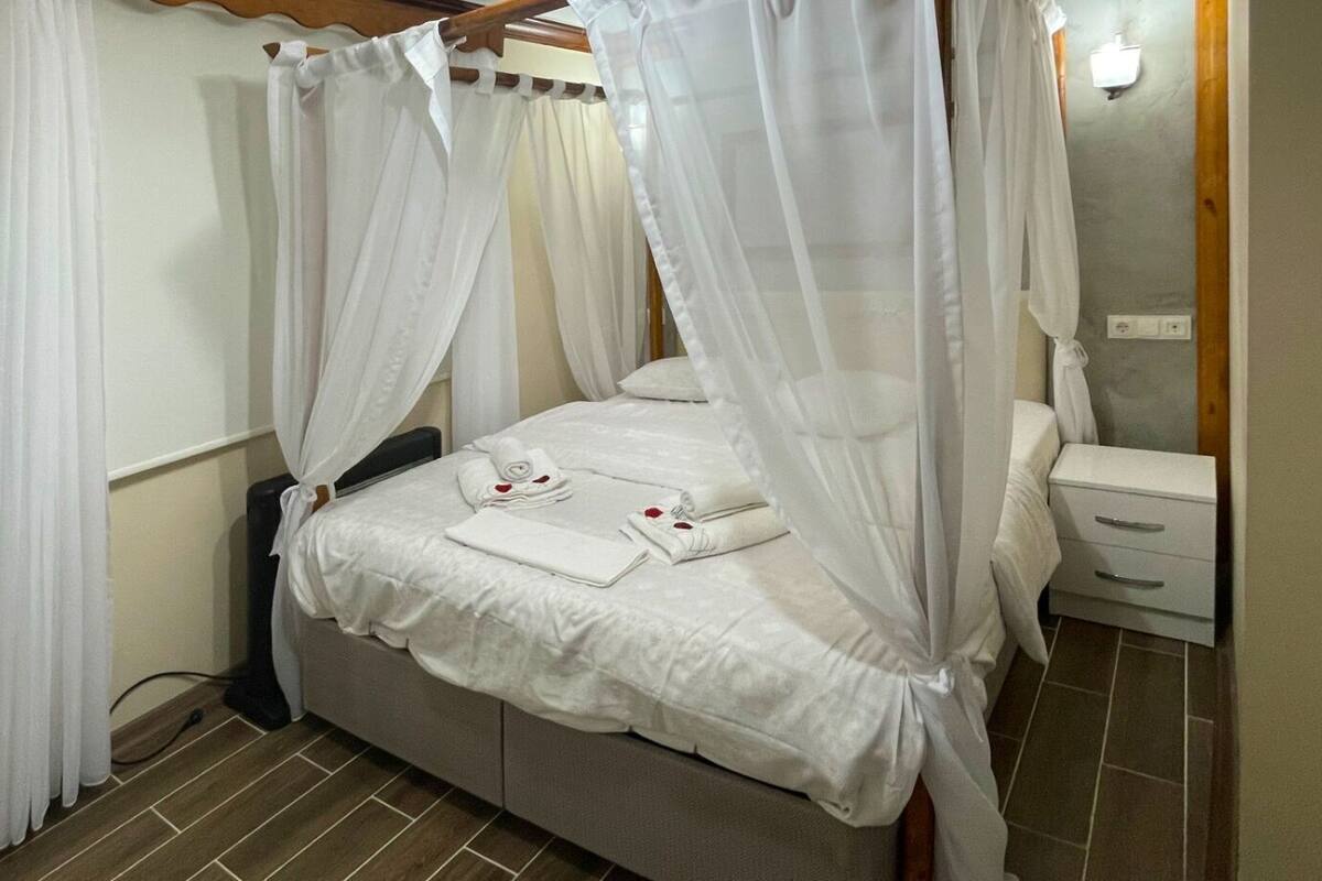 A bedroom with a four-poster canopy bed, a bedside table, a mirror, and a guitar.