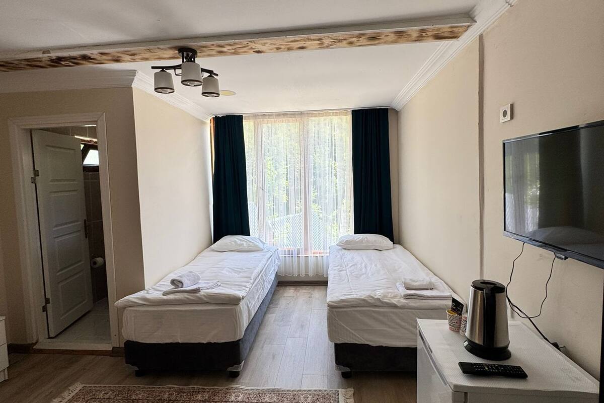 A hotel room with two single beds, a TV, a coffee maker, and a large window with curtains.