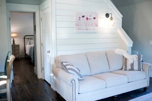 A room with a white sofa, a bed, a nightstand, and a wall-mounted light fixture. - Mtn Cabin Lake | Kayak | Fish | AtvTrls (MENA)