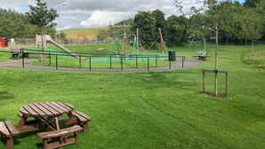 A park with a picnic table, playground equipment, and a green play area.