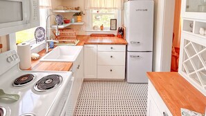 A compact kitchen with a stove, sink, and refrigerator, featuring a patterned floor and wooden countertops. - Vintage Cottage in Wanchese (Wanchese)