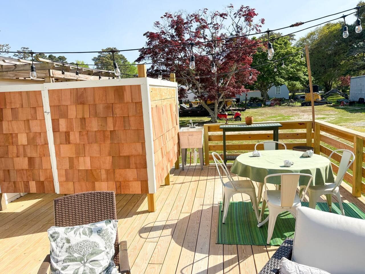 An outdoor deck with a table and chairs, a wooden fence, and a tree with red leaves.