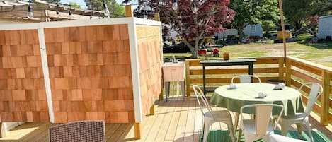 Een terras buiten met een tafel en stoelen, een houten omheining en een boom met rode bladeren.