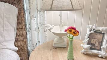 A round wooden table with a white lamp, a vase with flowers, and a picture frame.