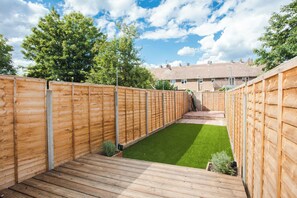 A wooden deck with a grassy area and a brick building in the background.