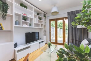 A modern living room with a flat-screen TV, white shelving, and a glass coffee table.