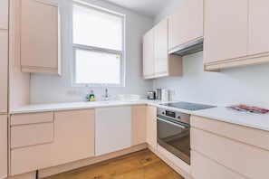 A modern kitchen with white cabinets, a double sink, a toaster, and an oven. - Stylish Modern 3 BDR Flat NW London Garden (London)