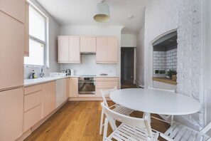 A modern kitchen with wooden flooring, white cabinets, and a round dining table with chairs. - Stylish Modern 3 BDR Flat NW London Garden (London)
