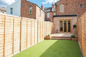 A residential backyard with a wooden fence, a small lawn, and a brick house with a glass door.