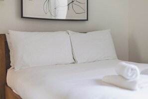 A neatly made bed with white linens and a rolled towel on the right side.