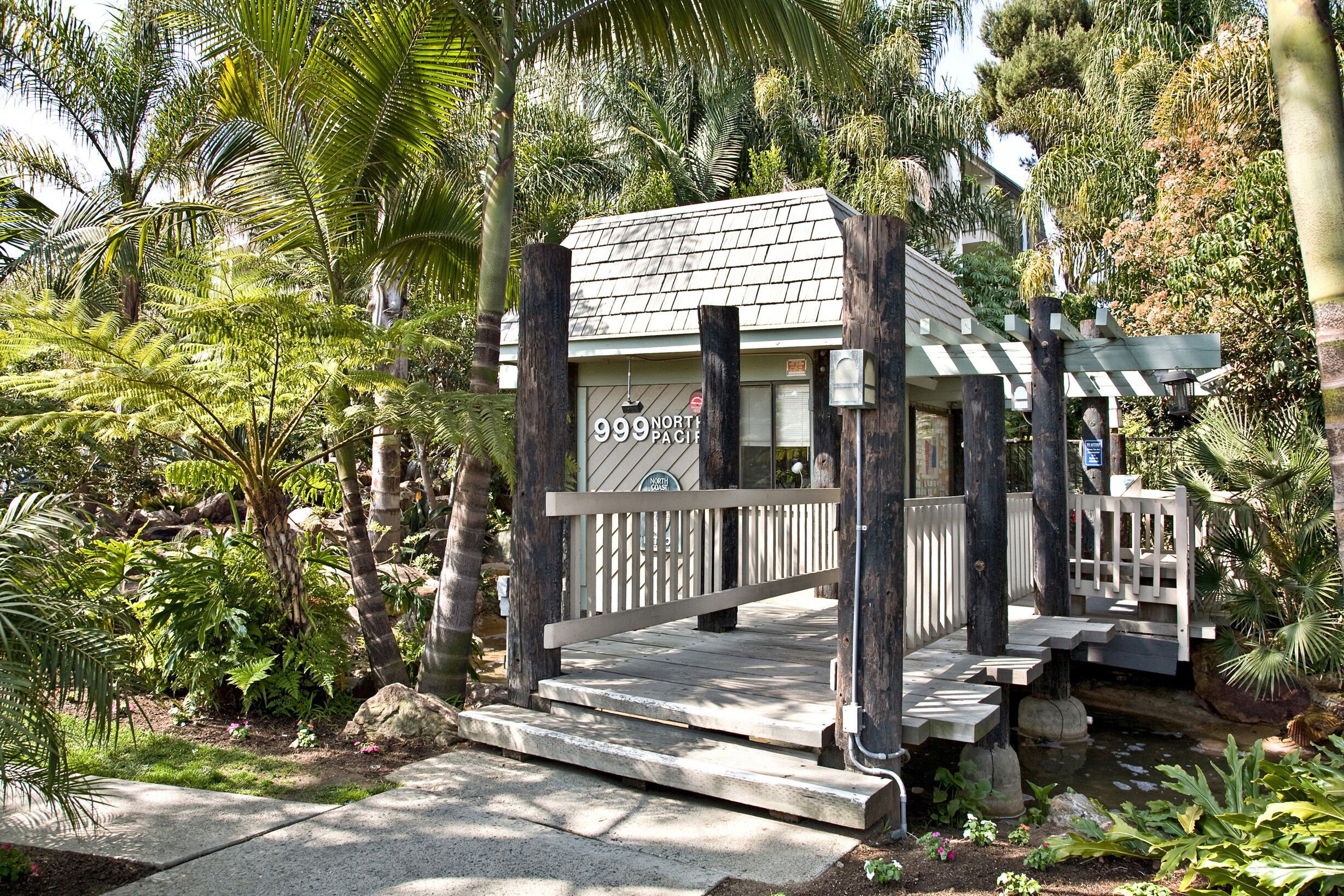 A small, rustic building with a sign reading "999 North Pacific" surrounded by lush greenery and a stone pathway.