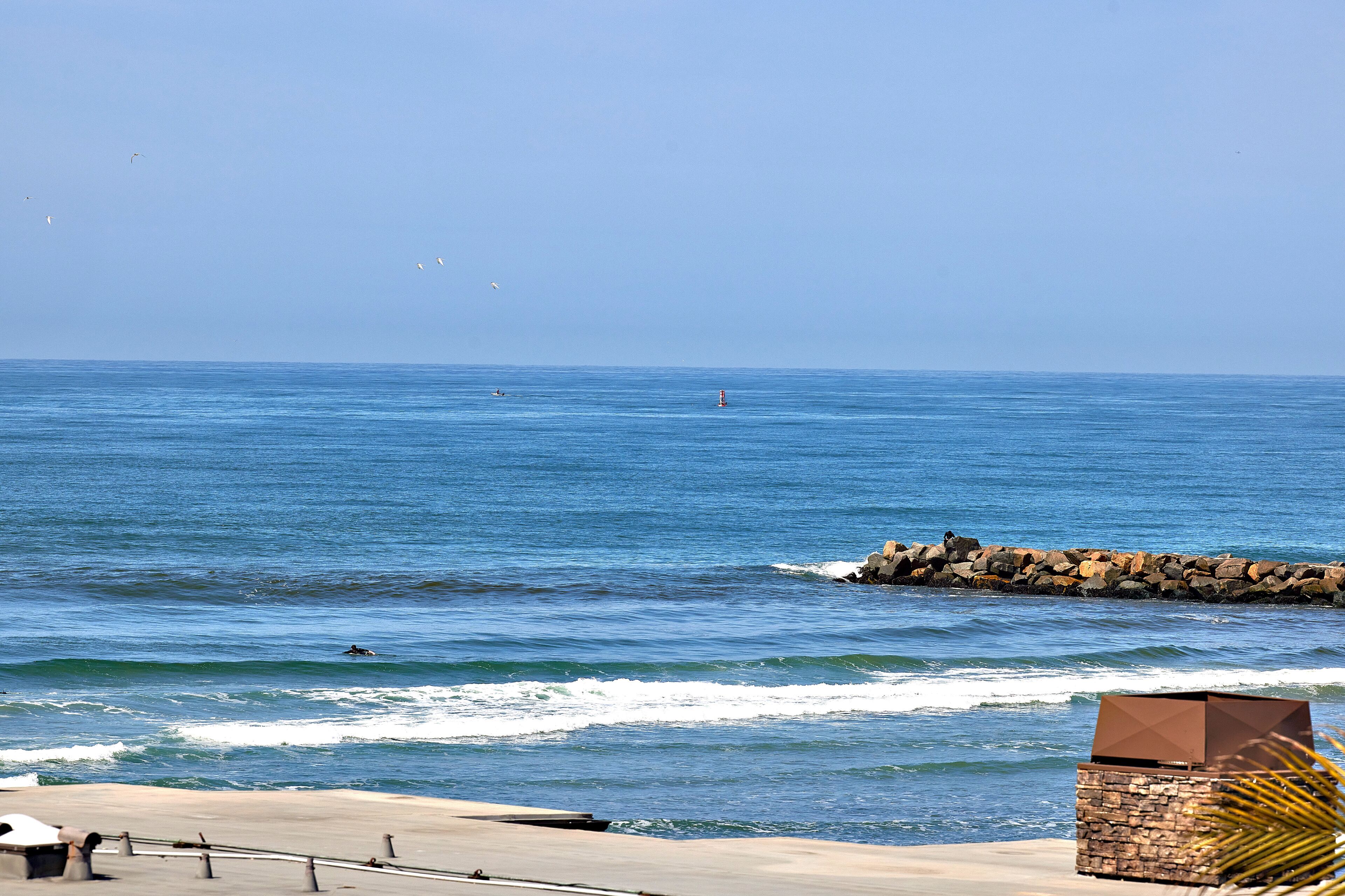 A coastal view with a clear sky, calm sea, and a rocky breakwater.