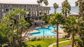A resort with a swimming pool, palm trees, and a view of the ocean.