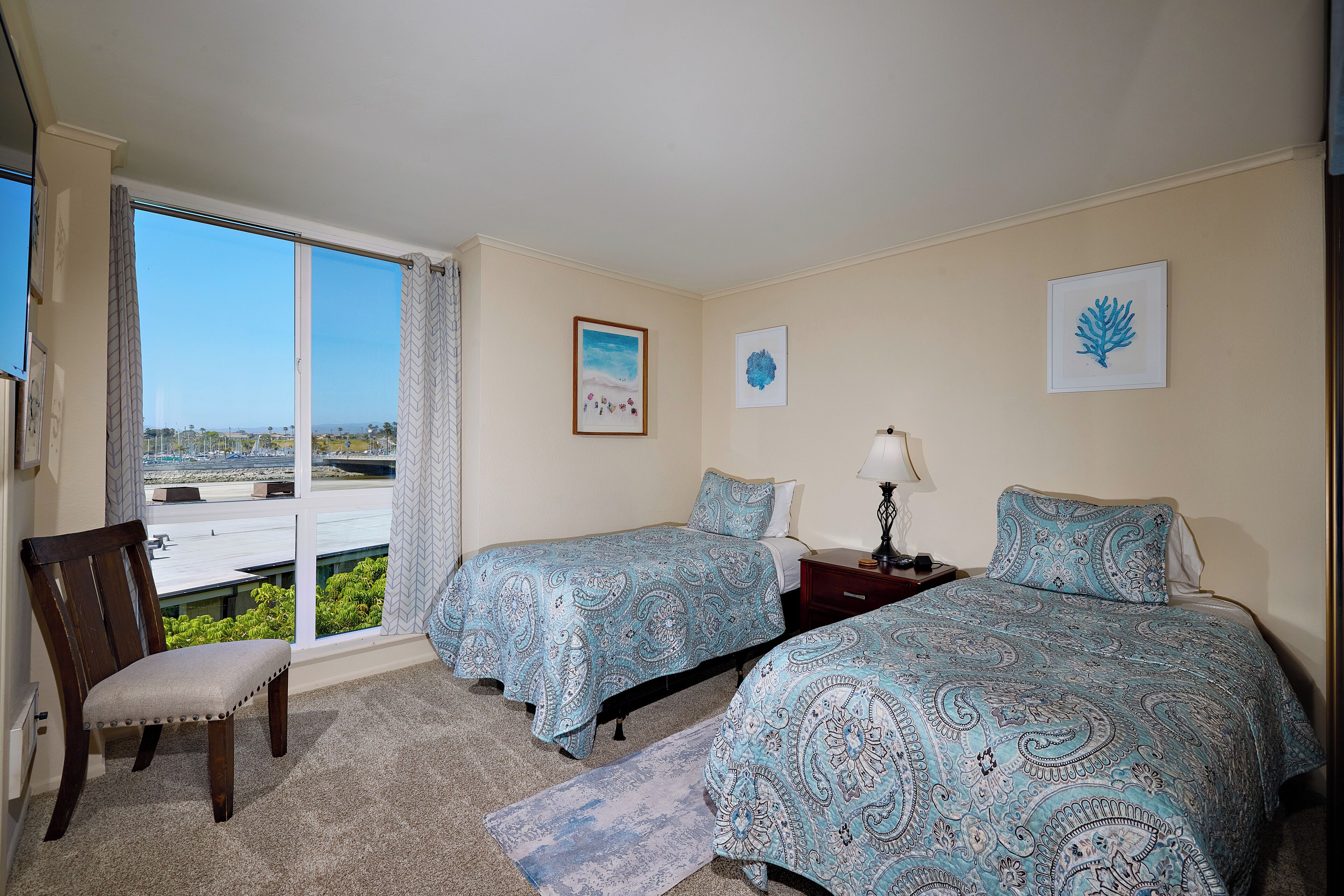 A bedroom with two beds, a chair, and a view of the outdoors.