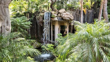 A lush garden with a waterfall, a wooden structure, and dense tropical foliage.