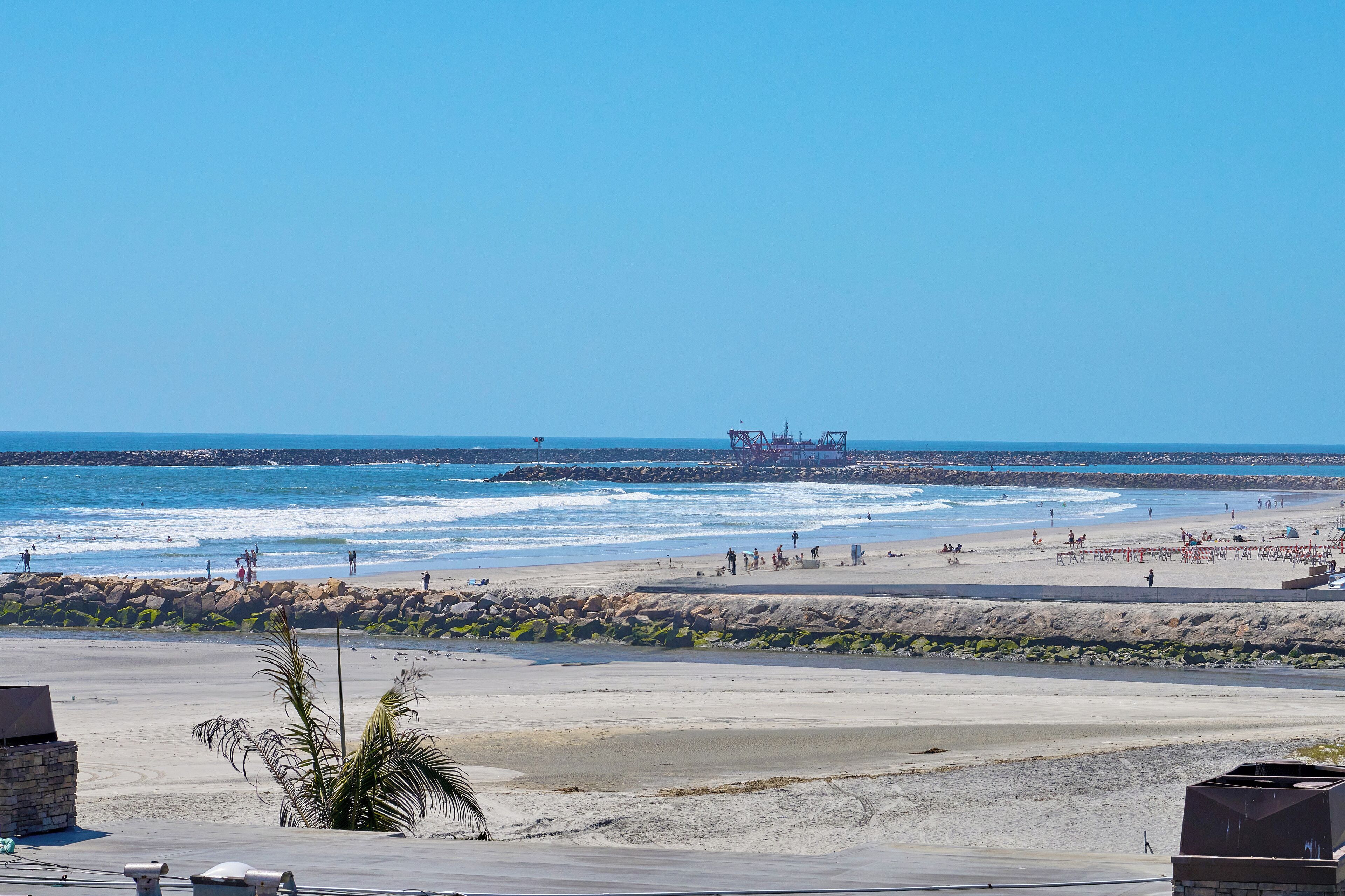 A beach with a rocky shoreline, waves, and a distant industrial structure.