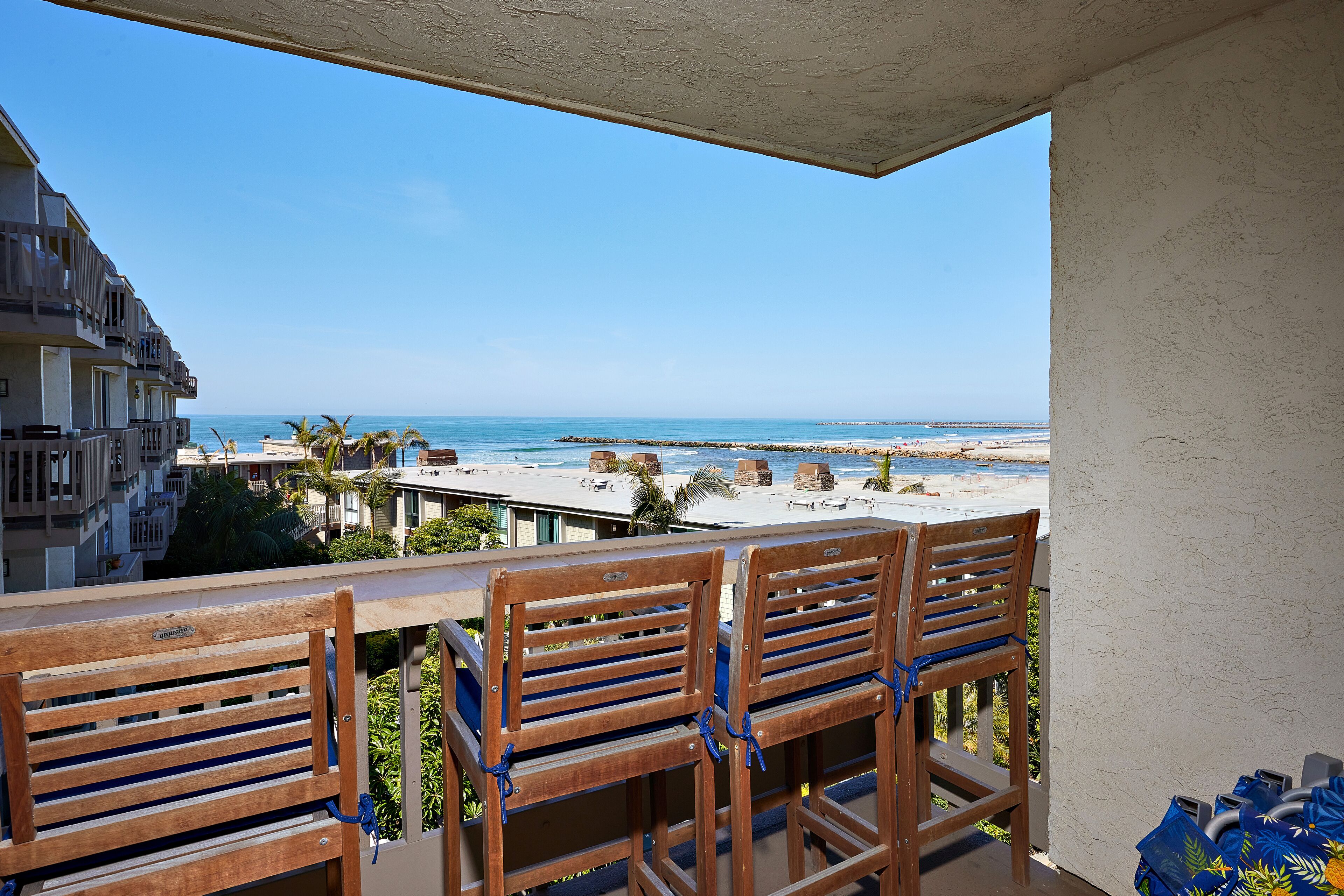 A balcony with wooden chairs, a view of the beach, and a building in the background.