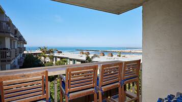 A balcony with wooden chairs, a view of the beach, and a building in the background.