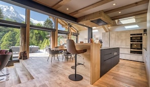 A modern kitchen with a wooden island, large windows, and a view of mountains.