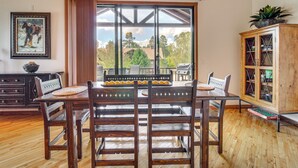 Uma área de refeições com mesa e cadeiras de madeira, uma janela com vista, um armário com portas de vidro e um quadro na parede.