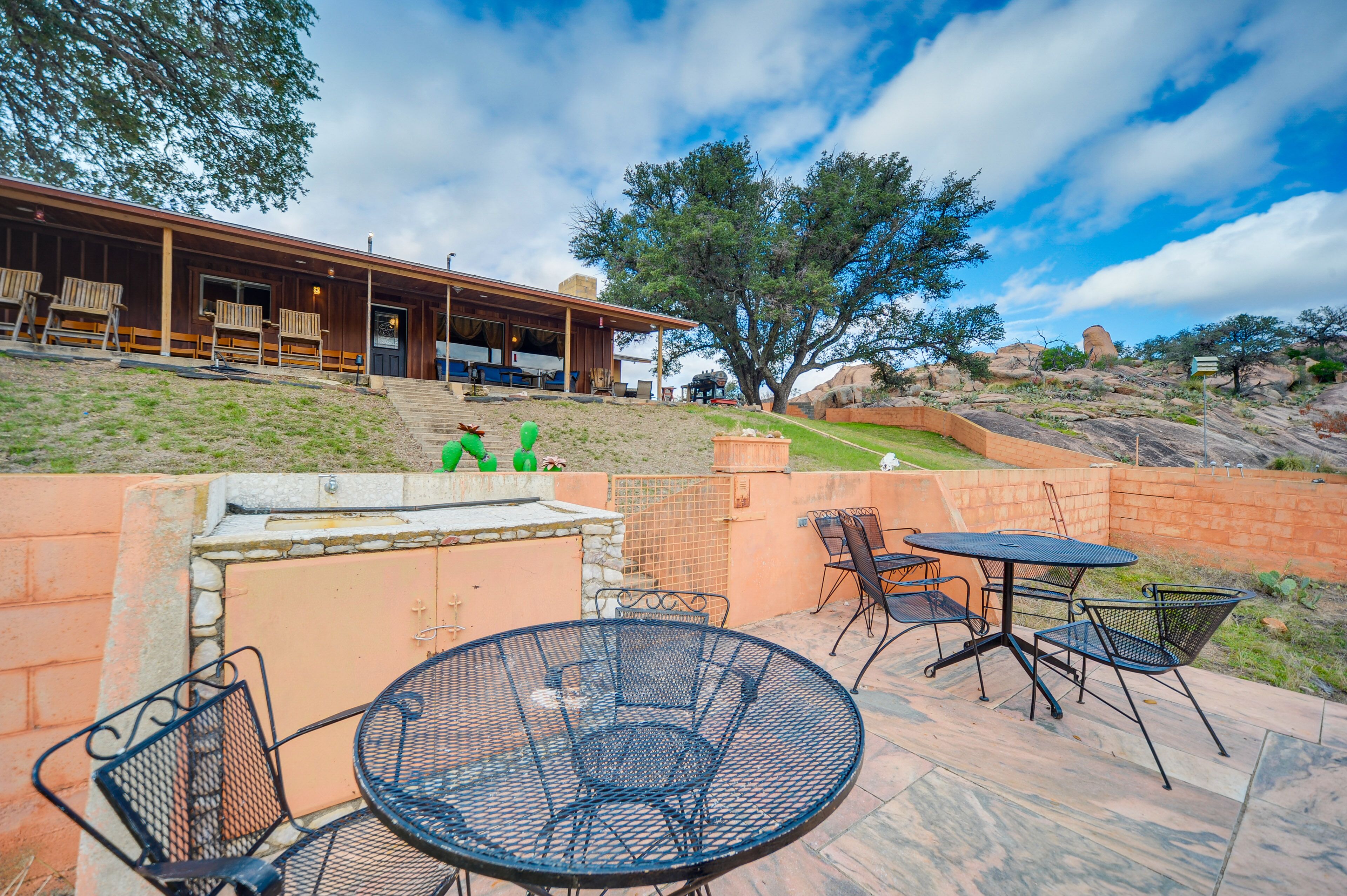 An outdoor patio with a round table and chairs, a barbecue grill, and a building with a covered porch.
