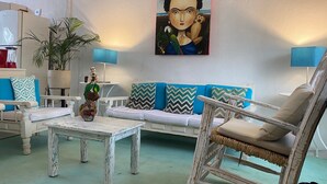 Un soggiorno con un divano bianco, cuscini a motivi blu e bianchi, un tavolino da caffè bianco e una poltrona rustica. Si nota un quadro appeso alla parete e una pianta in vaso nell'angolo.