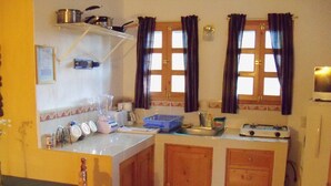 A compact kitchen with wooden cabinets, a sink, a stove, and a window with curtains.