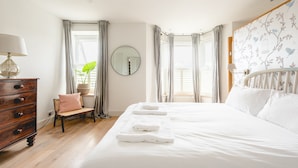 Une chambre à coucher avec un grand lit, une commode en bois, une chaise, un miroir et une fenêtre avec des rideaux.