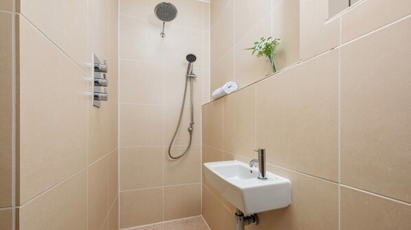A bathroom with beige tiles, a shower, a sink, and a small plant on the wall. - Treloweth, a large family home with sea views, parking and outside space, free WifI. (St Ives)