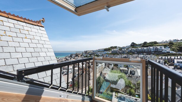 Un balcon donnant sur une ville côtière, un mur de briques et un ciel dégagé.
