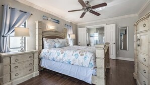 Ein Schlafzimmer mit einem Bett, einem Schminktisch, einem Deckenventilator und einem Fenster mit Vorhängen.