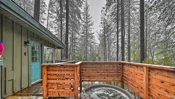 Une terrasse en bois avec un jacuzzi, une porte bleue et une vue sur de grands arbres.