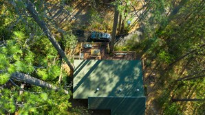 Vue aérienne d’une cabane surmontée d’un toit végétalisé, entourée d’une forêt dense.