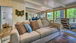 Un salon chaleureux avec un canapé beige, un plancher en bois et de grandes fenêtres donnant sur l’extérieur.