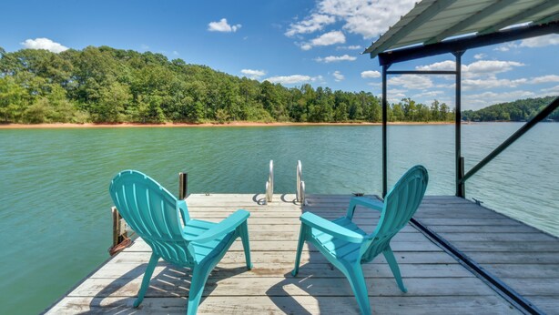 A wooden dock with turquoise chairs facing a calm lake, surrounded by lush greenery and a clear sky. - Spacious Lake Hartwell Home w/ Private Boat Dock! (Anderson)
