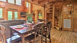 Ein Holzhütten-Interieur mit Essbereich, Kamin, Fernseher und Wendeltreppe.
