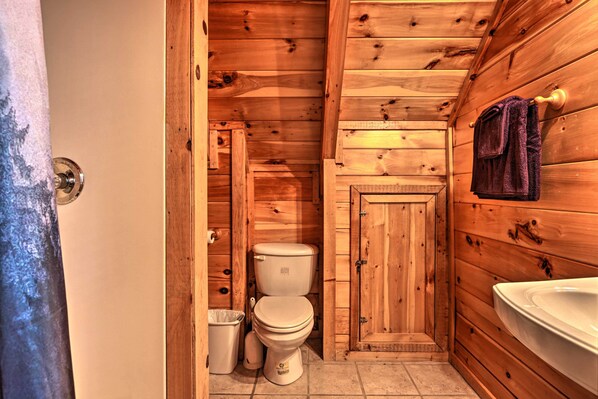 A wooden cabin bathroom with a toilet, sink, and a towel hanging on the wall. - 'Sky Harbor' Sevierville Cabin w/ Hot Tub & Deck! (Pigeon Forge)