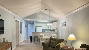 A living room with a sofa, a coffee table, and a lamp. There is a kitchen area with a refrigerator and a dining table.