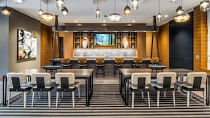 En modern hotellobby med en central bardisk, flera olika sittgrupper och hängande lampor.