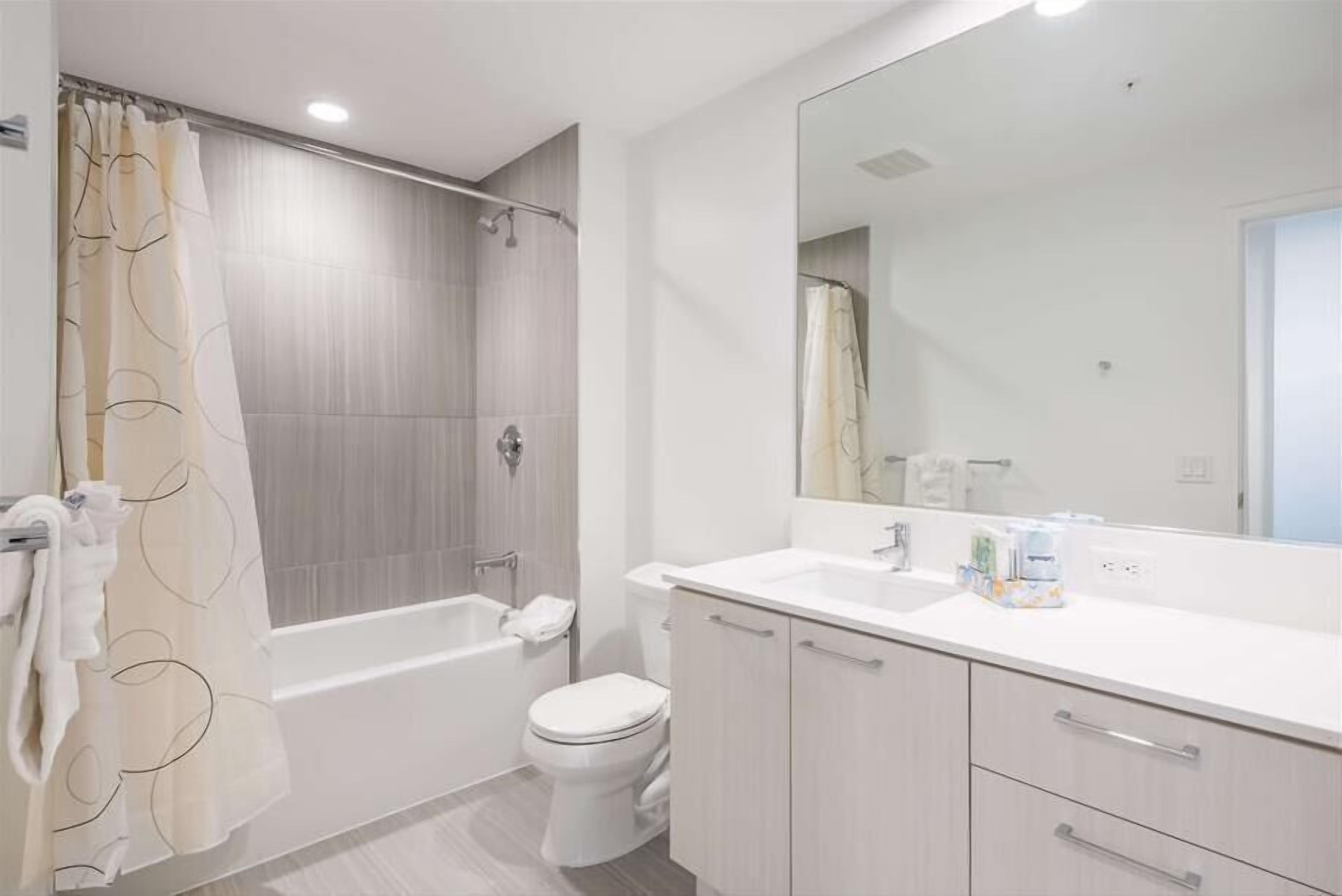 A modern bathroom with a bathtub, toilet, and vanity with a large mirror.