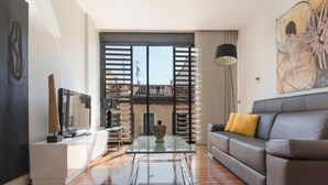 Un salon moderne avec une table basse en verre, un canapé en cuir agrémenté d’un coussin jaune, un téléviseur à écran plat posé sur un meuble et un grand tableau abstrait accroché au mur.