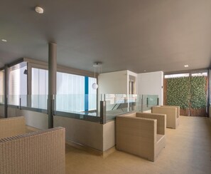 A modern interior with wicker furniture, a glass railing, and a view of the city.