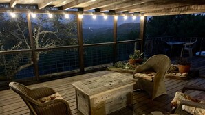 A covered outdoor seating area with wicker furniture, a wooden table, and a view of the surrounding landscape.
