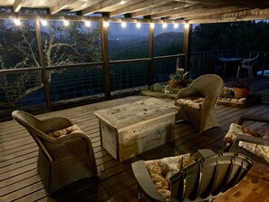 A covered outdoor seating area with wicker furniture, a wooden table, and a view of the surrounding landscape.