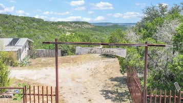 A gated entrance to a property named 'La Vista' with a dirt path leading inside, surrounded by greenery and hills in the background.