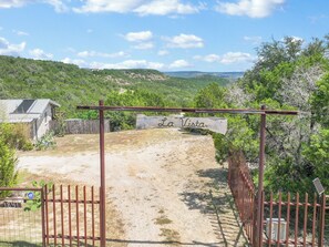 A gated entrance to a property named 'La Vista' with a dirt path leading inside, surrounded by greenery and hills in the background.