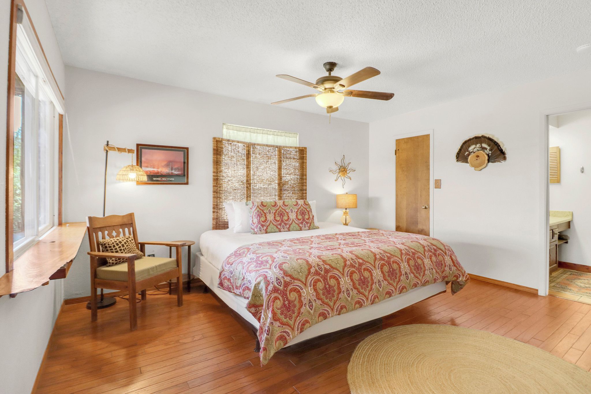 A bedroom with a bed, a chair, a ceiling fan, a window, and a door.