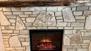 A stone fireplace with a fire, a wooden log, and a stone mantle.