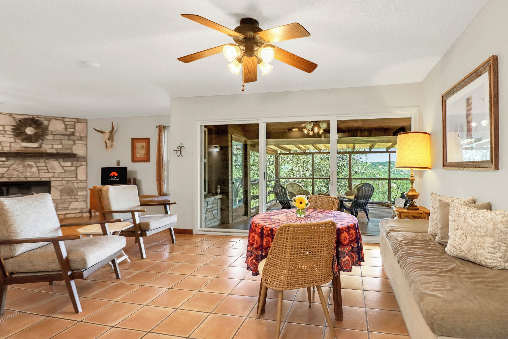 A living room with a fireplace, a ceiling fan, a dining table with chairs, and a sofa.