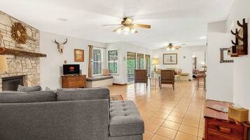 A spacious living room with a grey sectional sofa, a stone fireplace, and a ceiling fan.